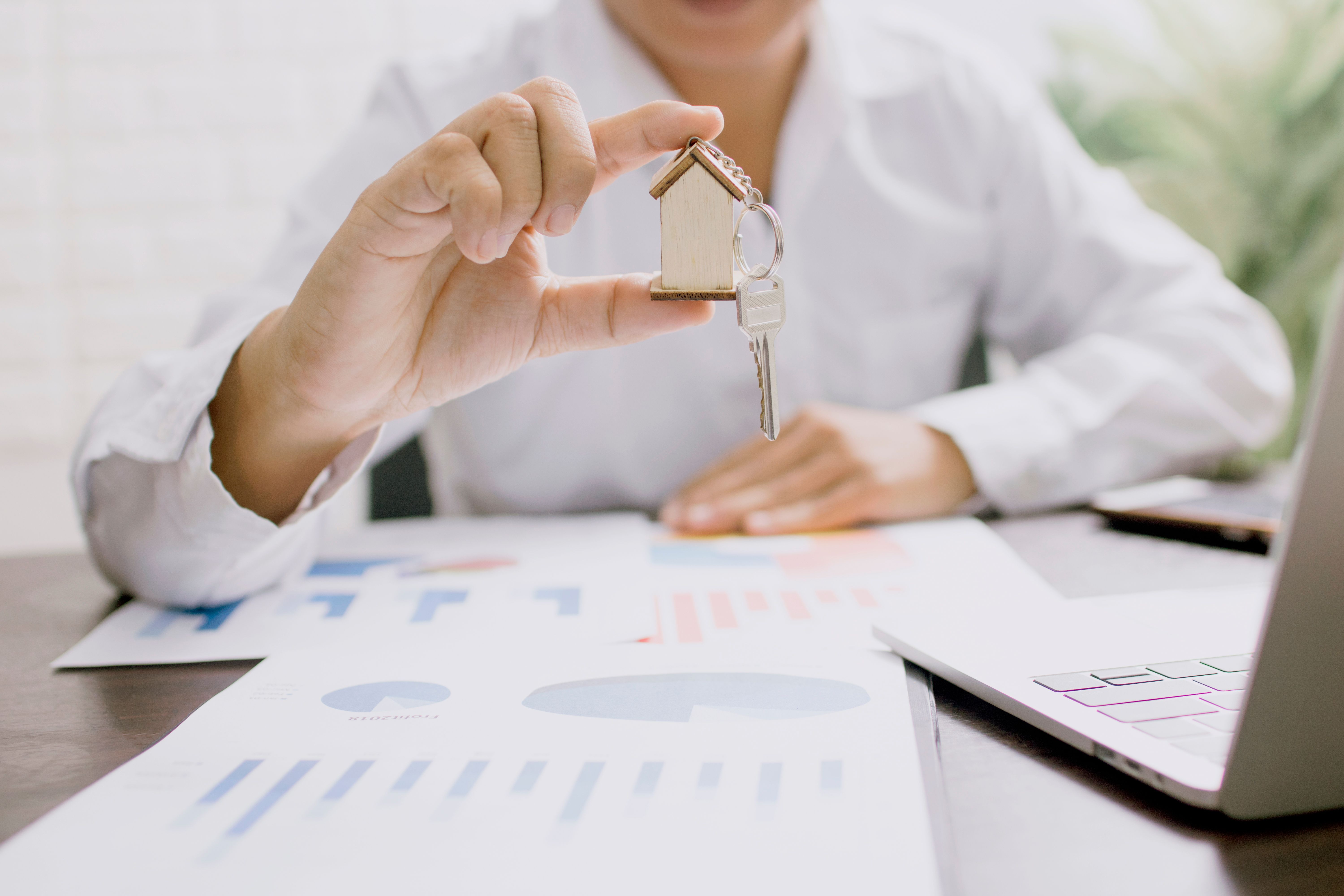 A person holding up a house-shaped keyring with financial documents on the desk in front of them.